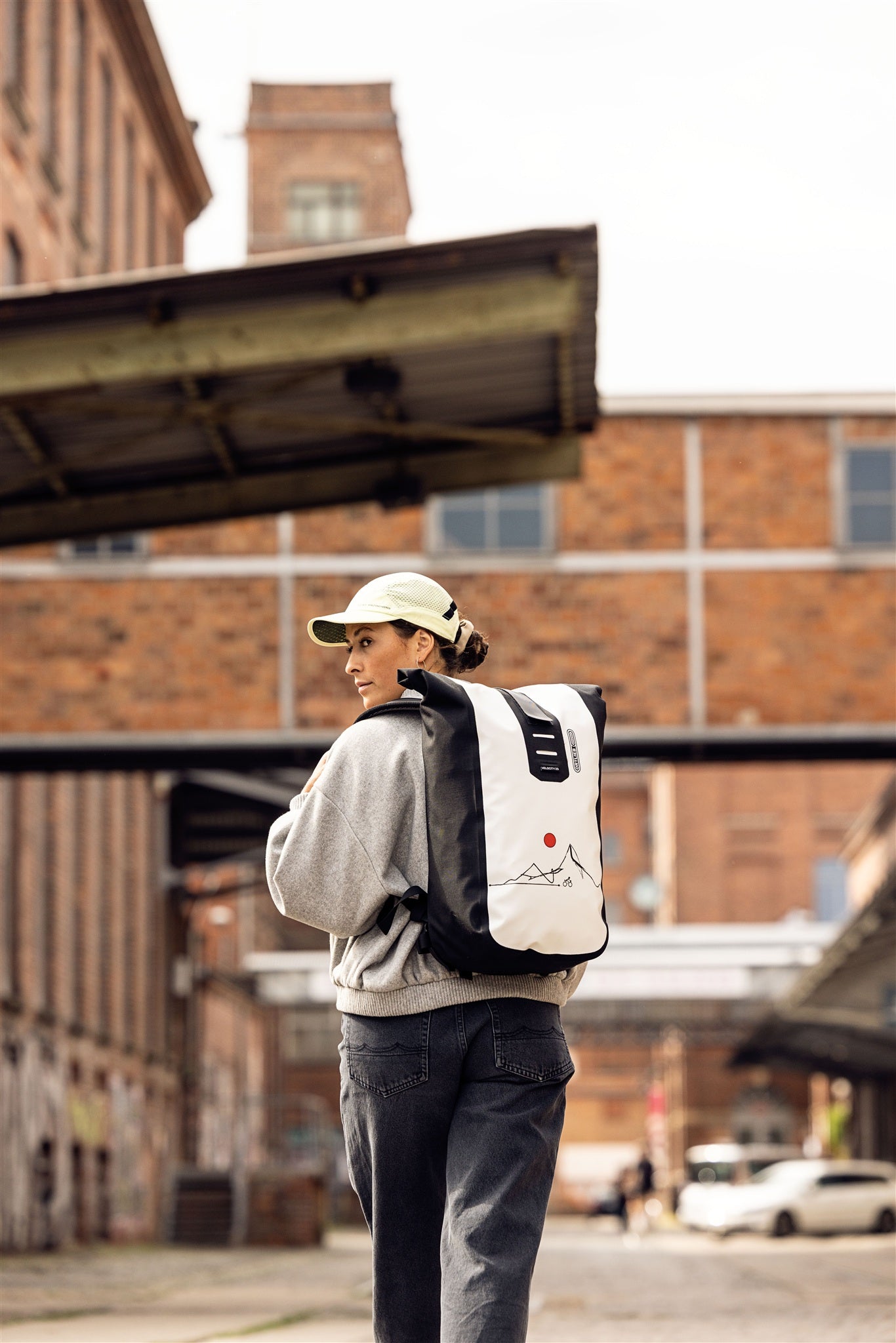 Woman wearing ORTLIEB Velocity Design backpack in industrial area with brick buildings