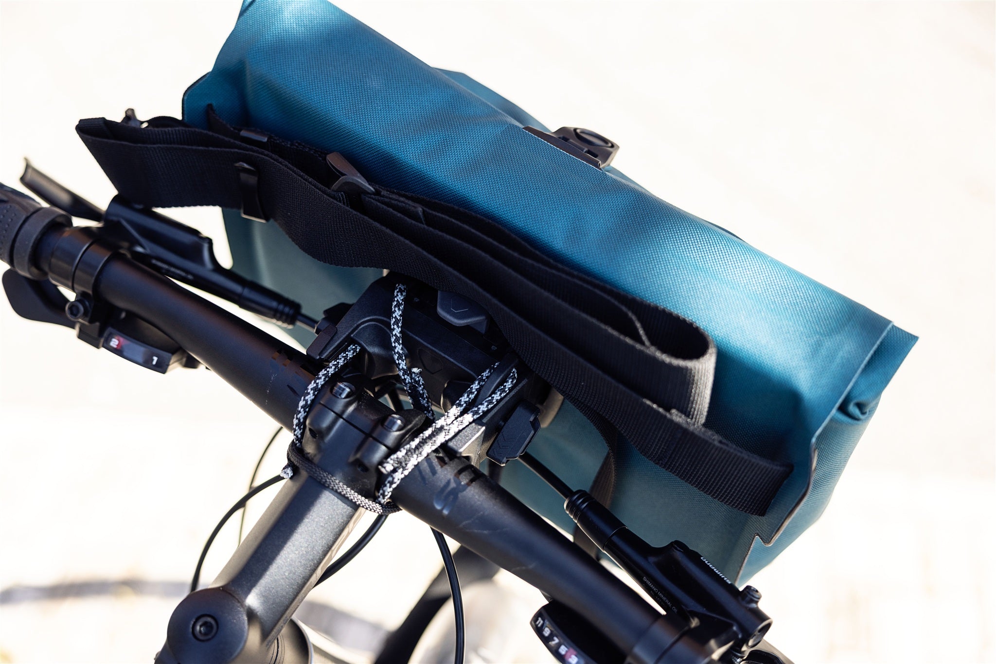 Detailansicht der petrolfarbenen ORTLIEB Velo-Sling Flex Lenkertasche mit Bar-Lock-Halterung aus wasserdichtem Gewebe am Fahrradlenker.