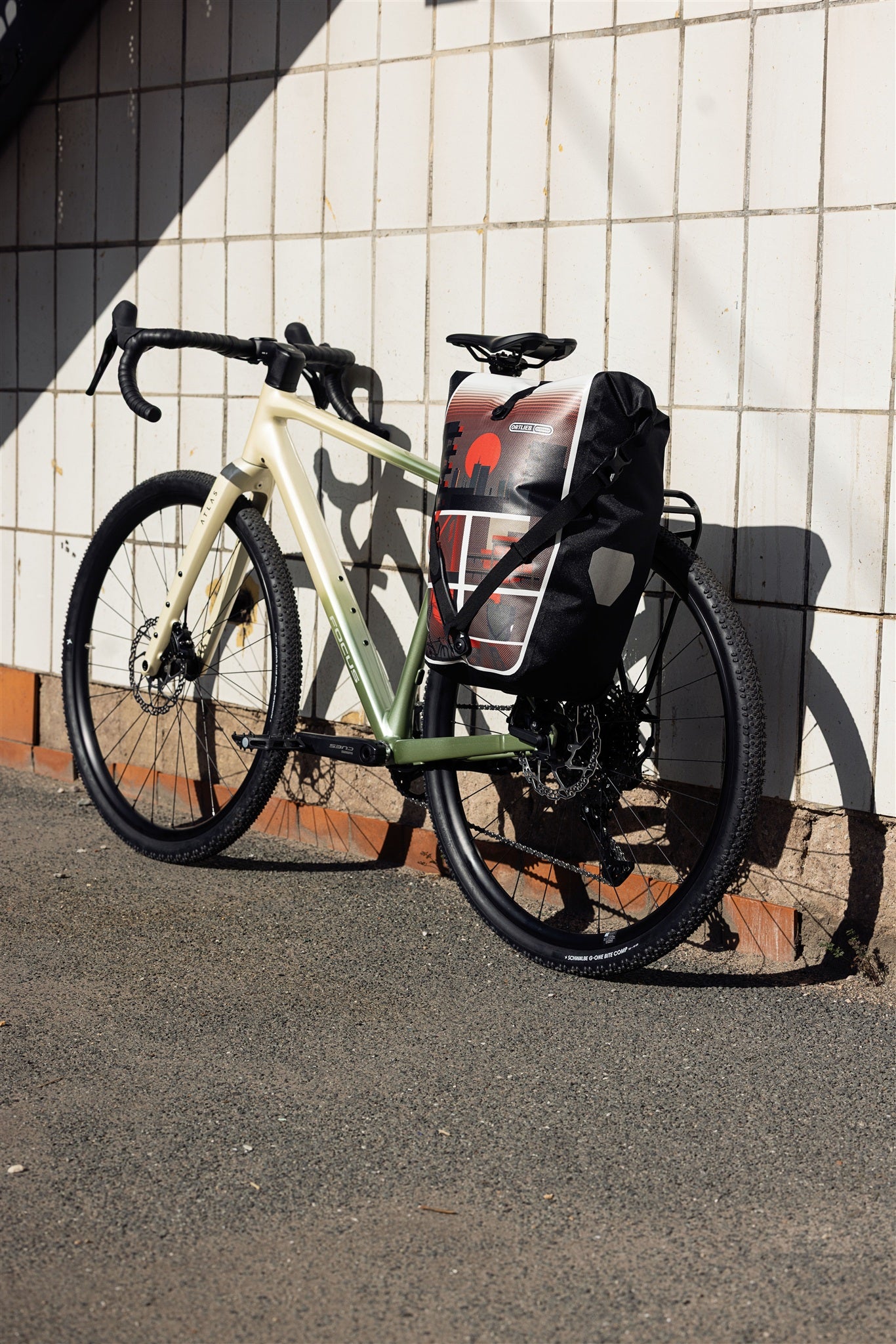 Woman with helmet stands by wall next to bicycle with ORTLIEB Back-Roller Design bag in design "Morning Routine"